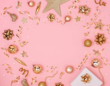 Süslemeli Noel kompozisyonu ve altın yaylı hediye kutusu ve pembe pastel arka planda yıldız konfetisi. Kış, yeni yıl konsepti. Düz konum, üst görünüm, kopyalama alanı.