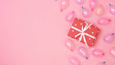 Süslemeli ve balonlu hediye kutusu kompozisyonu, pembe pastel arka planda konfeti. Doğum günü, yeni yıl konsepti. Düz konum, üst görünüm, kopyalama alanı.