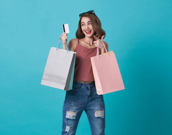 Porträtt av en lycklig ung kvinna som visar kreditkort och shoppingväska isolerad över Blå bakgrund. — Stockfoto