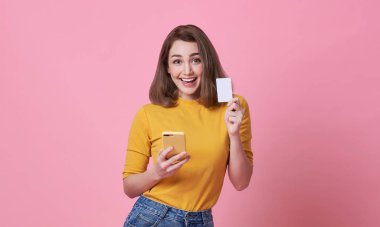 Pembe arka planda cep telefonu ve kredi kartı tutan heyecanlı genç kadın..
