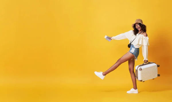 Heureuse femme africaine souriante vêtue de vêtements d'été avec des bagages profitant de leurs vacances d'été escapade en fond de bannière jaune avec espace de copie . — Photo