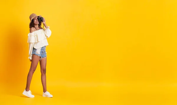 Joyeux jeune femme africaine vêtue de vêtements d'été tenant caméra tir sur fond jaune avec espace de copie . — Photo