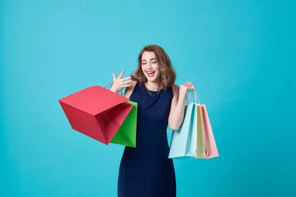 Lycklig vacker ung kvinna i blå klänning och hand hålla shoppingväska isolerade över Blå bakgrund. — Stockfoto