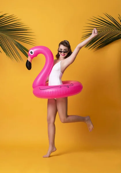 Feliz mujer sonriente vestida con traje de baño sosteniendo anillo de goma flamingo y disfrutando de su escapada de vacaciones de verano en fondo amarillo . — Foto de Stock