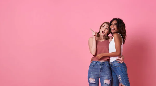 Retrato de duas jovens excitadas de pé com o dedo apontando para o espaço de cópia isolado sobre fundo de banner rosa com espaço de cópia . — Fotografia de Stock