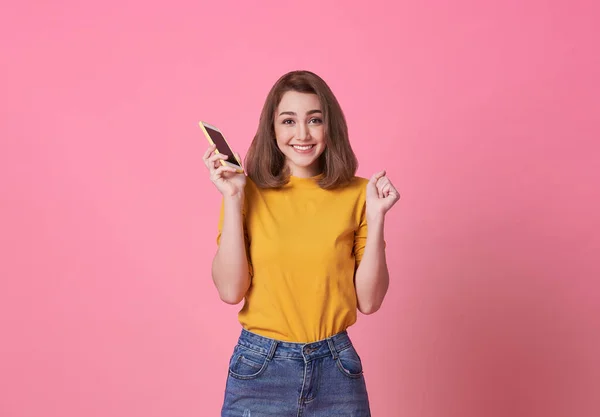 Pembe arka planda cep telefonu tutan mutlu genç kadın portresi.