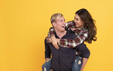 Heyecanlı genç çift eğlenirken bir adam sarı arka planda kız arkadaşını sırtında taşıyor..