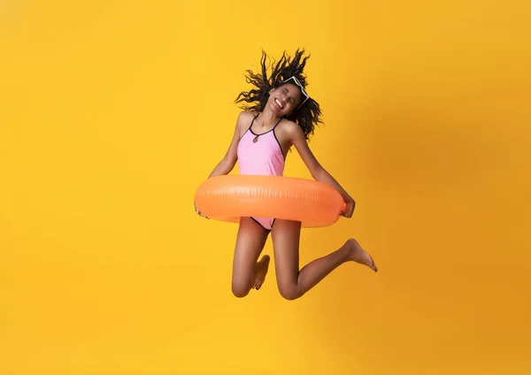 Glad ung kvinna klädd i badkläder med gummiring och hoppa på gul bakgrund. — Stockfoto