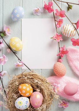 Mutlu Paskalyalar, sahte kağıt kartlar ve tahta masadaki yuvada boyanmış Paskalya yumurtaları. Kopyalama alanı olan üst görünüm.