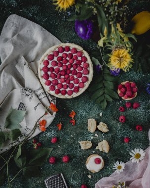 Frambuazlı pasta ve çiçekler karanlık yüzeyi.