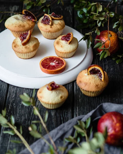 Muffins with blood oranges on black wooden table