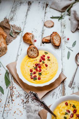 Kızarmış ekmekli balkabağı kreması çorbası, eski püskü beyaz arka planda nar tohumu ve baharatlar, koni, tekstil ve otlar, üst görünüm