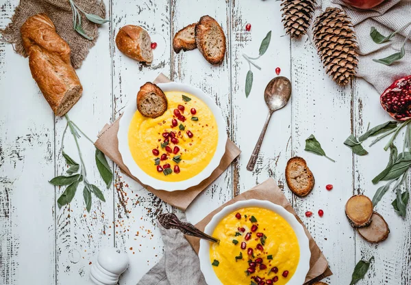 Kızarmış ekmekli balkabağı kreması çorbası, eski püskü beyaz arka planda nar tohumu ve baharatlar, koni, tekstil ve otlar, üst görünüm
