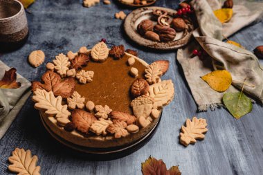 Geleneksel balkabağı turtası yapraklı kurabiyelerle süslenmiş eski püskü mavi arka planda tekstil ve şükran günü konseptiyle