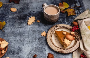 Eski püskü mavi arka planda yapraklı kurabiyelerle süslenmiş geleneksel balkabağı turtası. Kahve ve tekstil, Şükran Günü konsepti.