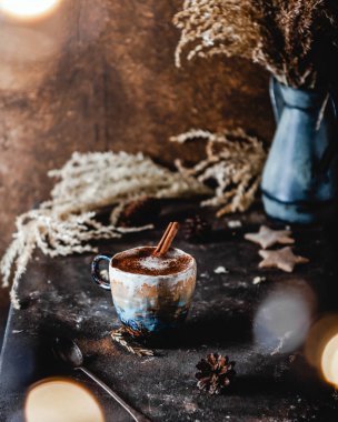 Kahverengi masada tarçın çubuklu bir fincan kahve ve çam kozalaklı kuru otlar, bayram kartı.