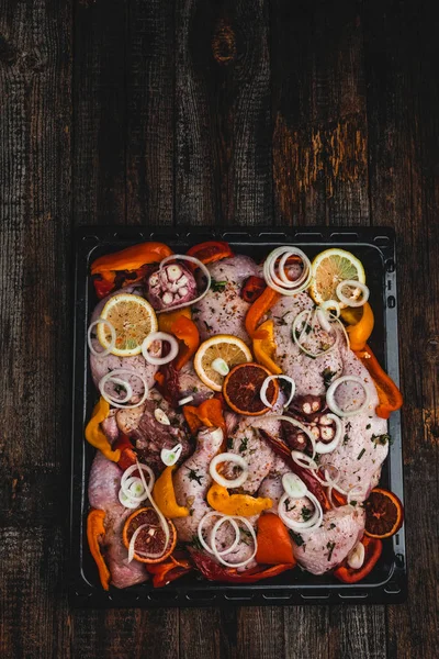 raw chicken legs marinated with dried fruits and vegetables on oven-tray, close view