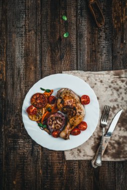 Kızarmış tavuk budu, sebzeli ve portakallı. Kahverengi ahşap masa üzerinde beyaz tabakta servis ediliyor.