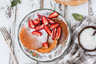 Krepli tabak ve şeker tozlu taze çilek. Tahta beyaz masa, kahvaltı konsepti.