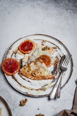 Ekşi kremalı kızarmış krep ve eski püskü gri arka planda kan portakalları, geleneksel kahvaltı konsepti.