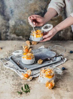  Kavanozlarda chia tohumları, mango dilimleri ve pejmürde bej arka planda çam fıstığı, sağlıklı kahvaltı konsepti.