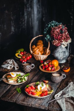 Haşlanmış yumurta ve sebzeli kahvaltı kaseleri. Kahverengi ahşap masada meyve ve fincanlar. 