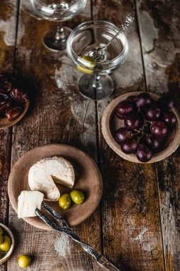 Peynirli ve üzümlü tabaklar ve martini bardaklı zeytinler ahşap arka planda