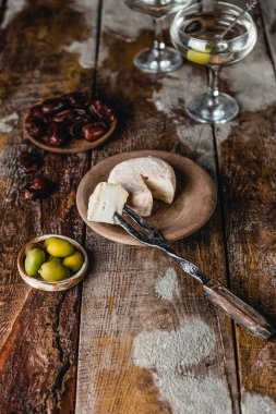 Peynirli tabaklar, hurmalar ve martini bardaklı zeytinler ahşap arka planda