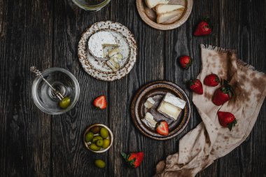 Peynirli ve çilekli tabaklar ve arkaplanda martini bardaklı zeytinler.