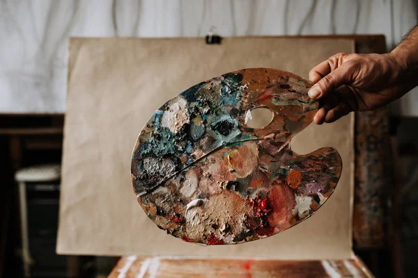 Painter holding palette of colors against canvas