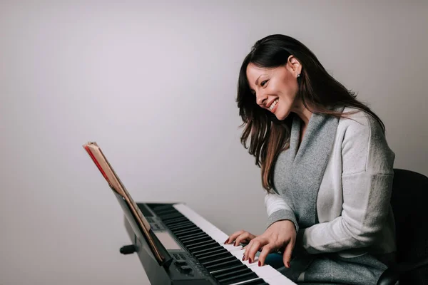 Smiling woman pianist playing synthesizer from sheet music