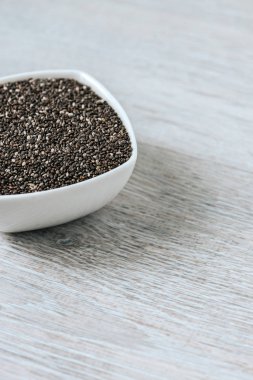 Dikey görüntü chia tohum ahşap bir masa üzerinde bir beyaz seramik kase.