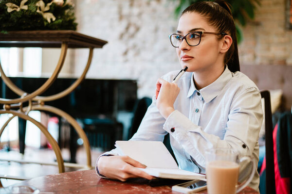 Contemplative woman thinking about idea for project. Making notes in the cafe.