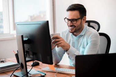 Ev ofis masasında çalışırken kahve fincanı tutan gülümseyen iş adamı