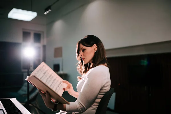 Image of female pianist sitting in front of a synthesizer holding sheet music.