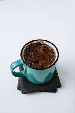 Dikey görüntü emaye kupa siyah coaster üzerinde siyah kahve. Beyaz arka plan.