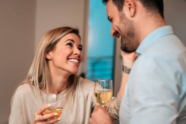 Genç çift, beyaz şarap içme ve evde gülüyor. Yakın çekim.