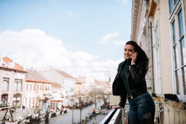 Kız balkonda dikilirken akıllı telefondan konuşuyor..