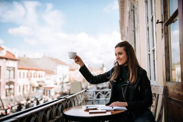 Girl sitting on the balcony inviting a friend for a cup of coffee.