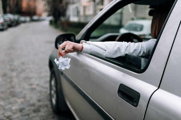 Female hand throwing trash out of car window.