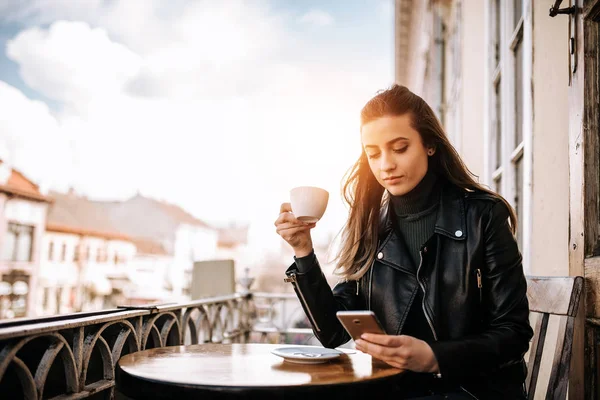 Girl using phone while enjoying a cup of coffee on the balcony over the city street.