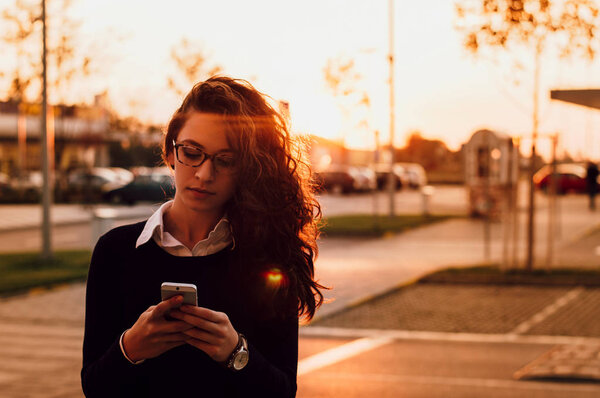 Young brunette woman using mobile phone outside on sunset.