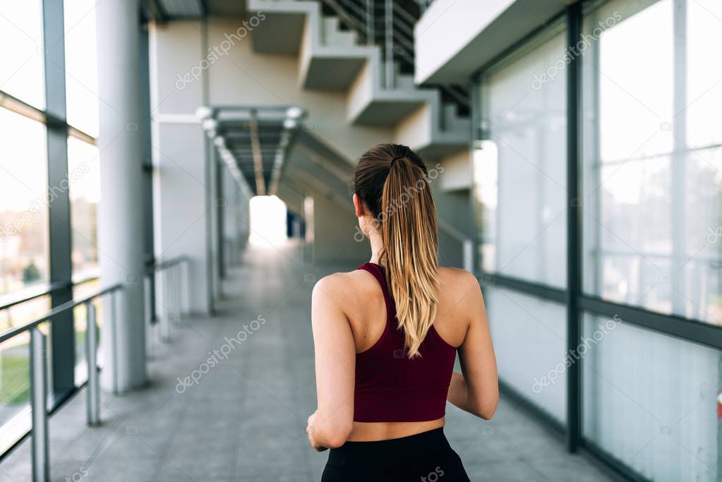 Rear view of young sports woman runner running indoors