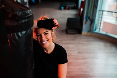 Kum torbasına yaslanmış bir gülümseyen kız portresi. Kameraya bakarak.