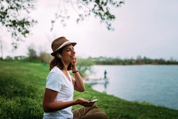 Mujer Joven Sonriente Escuchando Música Sentada Césped Parque Cerca Del — Foto de Stock