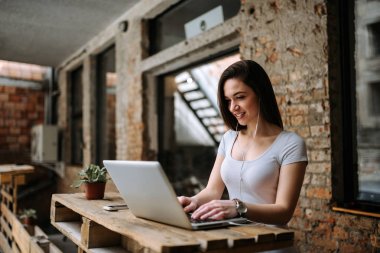 Dizüstü bilgisayar kullanarak earphones ile gülümseyen genç kadın.