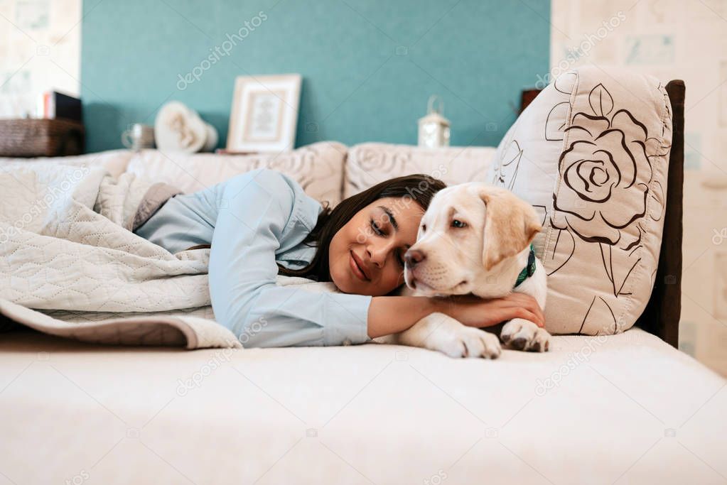 Attractive young woman with dog laying on bed  