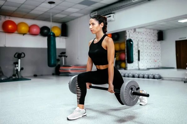 Attractive woman doing lunge exercise with barbell at gym