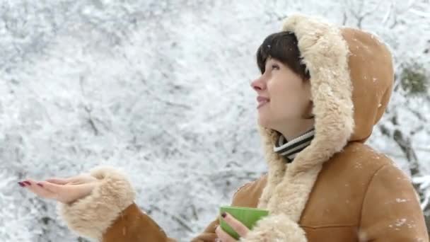 Een meisje met een kopje thee kijkt naar de vallende sneeuw in de winter. Zware sneeuwval. Mooie winter. — Stockvideo