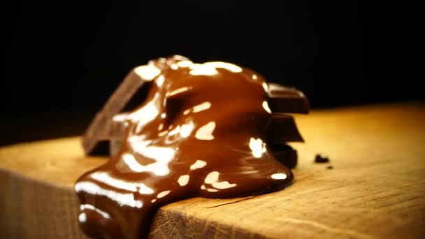 Pezzi di cioccolato fondente vengono versati con cioccolato fuso. Cioccolato liquido si diffonde e scorre lungo una tavola di legno — Video Stock